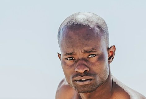 man sitting beside body of water holding white surfing board during daytime